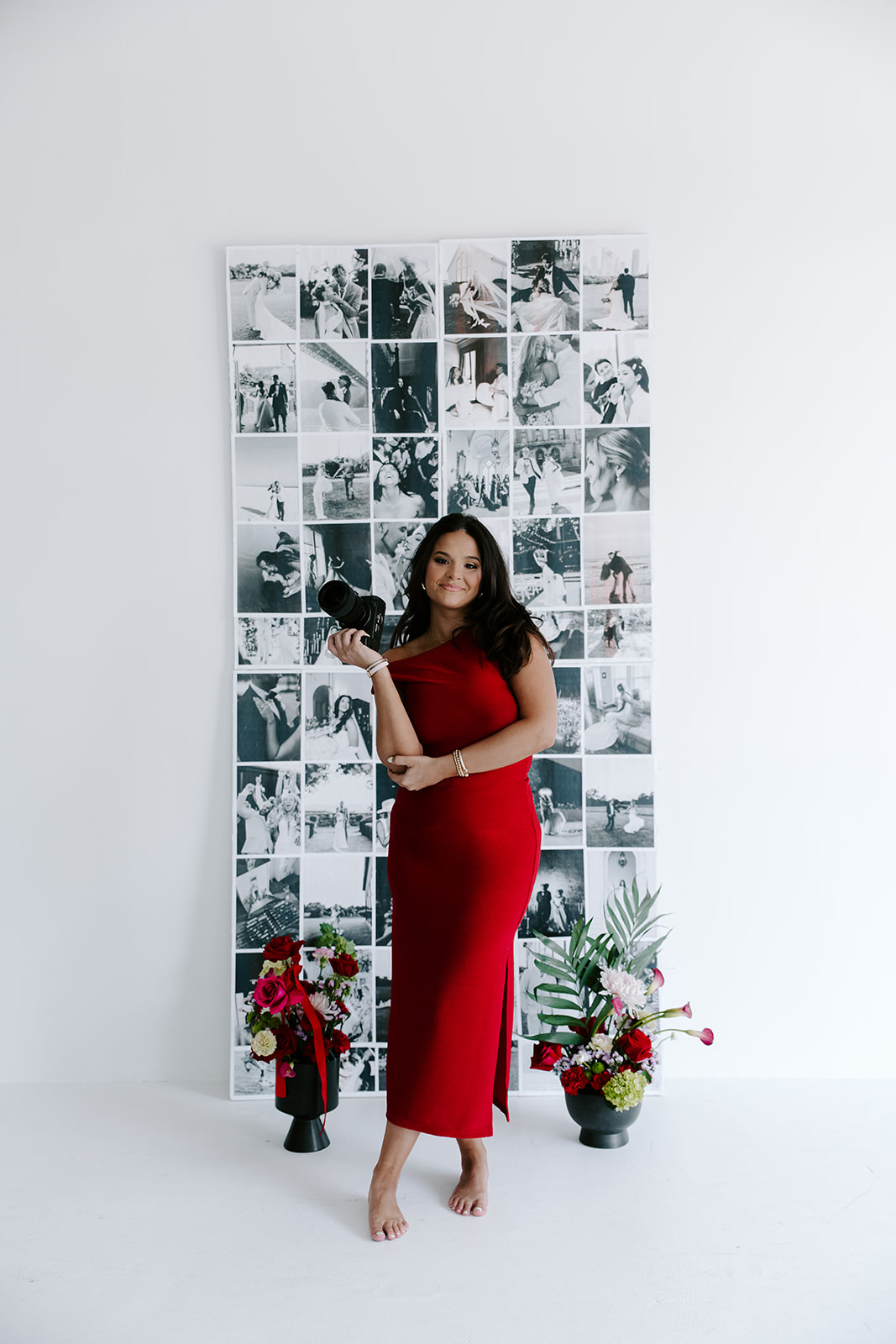 Lily in a red dress holding her camera in front of her photography display